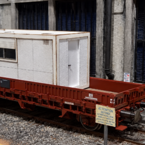 Bungalow préfabriqué INFRA 20 pieds à l’échelle HO, transporté sur wagon plat SNCF. Maquette en kit à monter et personnaliser, idéale pour représenter une base vie, un bureau de chantier ou un local technique sur un réseau ferroviaire.